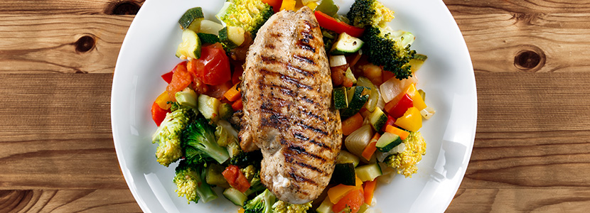 Grilled chicken fillet, breast with cooked vegetable Tomatoes, Carrots, Peppers, Courgettes, brocoli on plates.